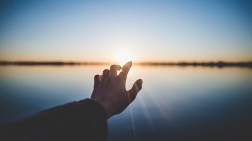 landscape photography of person's hand in front of sun