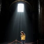 Unrecognizable man praying in church in sunlight